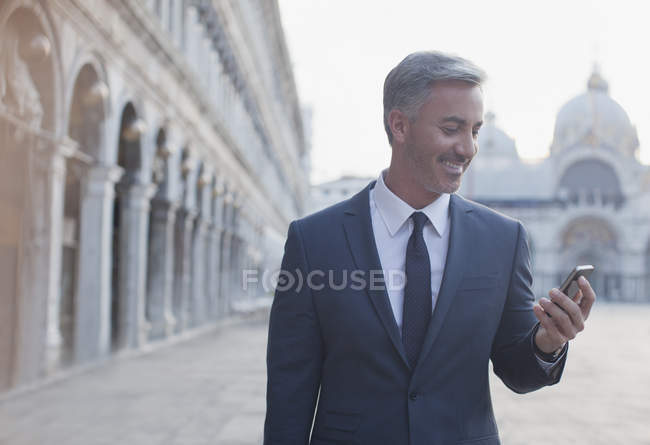 Hombre de negocios sonriente comprobando el teléfono celular en la Plaza de San Marcos en Venecia - foto de stock