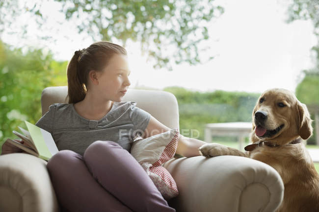 Mädchen entspannt sich mit Hund im Sessel im modernen Zuhause — Stockfoto