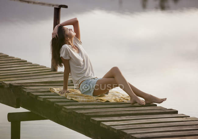 Mujer con la cabeza hacia atrás y la mano en el pelo en el muelle sobre el lago - foto de stock