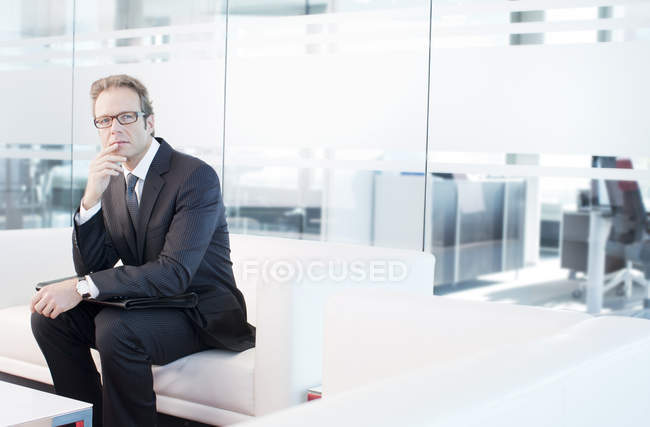 Empresario sentado en un sofá en el moderno vestíbulo de la oficina - foto de stock