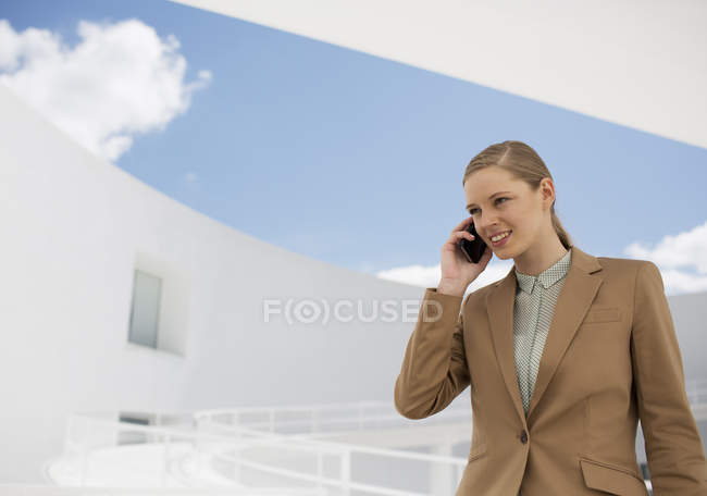 Femme d'affaires souriante parlant sur un téléphone portable dans la cour — Photo de stock