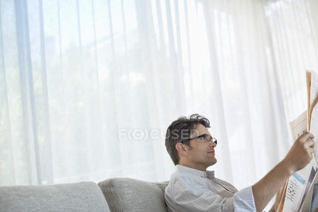 Hombre leyendo el periódico en el sofá - foto de stock