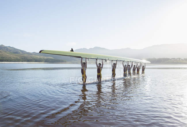 Rowing team holding scull overhead in lake — Stock Photo