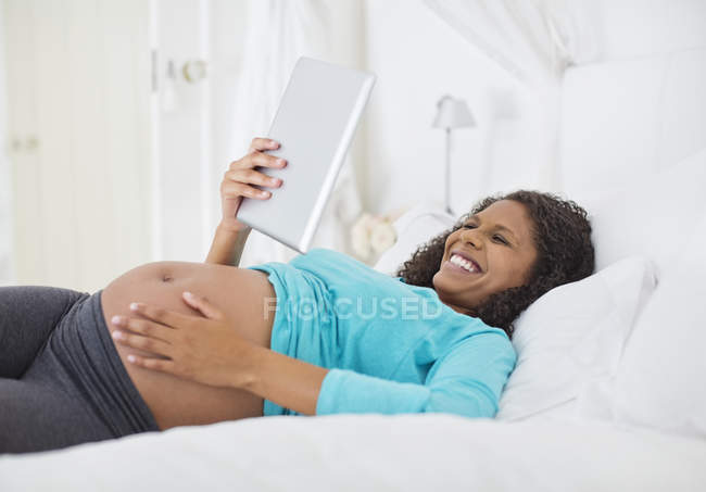 Беременная женщина с помощью планшетного компьютера на кровати — стоковое фото