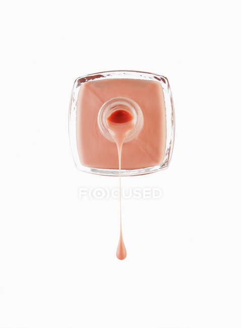 Закрыть персиковый лак для ногтей, капающий из бутылки — стоковое фото