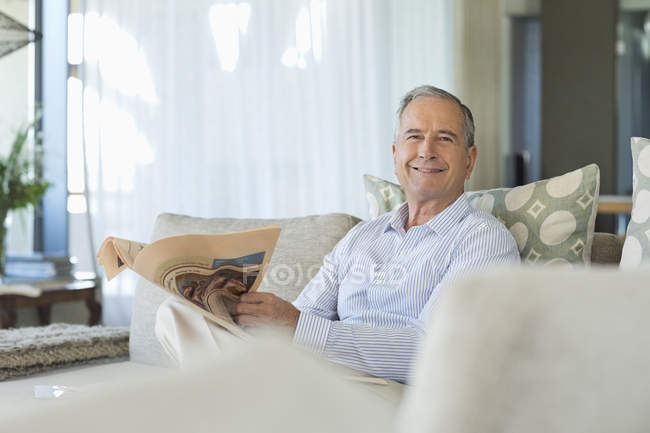 Older man reading newspaper on sofa — Stock Photo