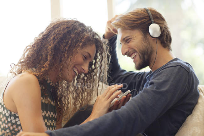 Jeune couple attrayant écoutant des écouteurs sur le canapé — Photo de stock