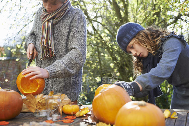 Crianças esculpindo abóboras juntas na mesa ao ar livre — Fotografia de Stock