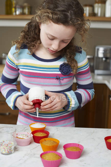Chica decorando cupcakes en la cocina - foto de stock