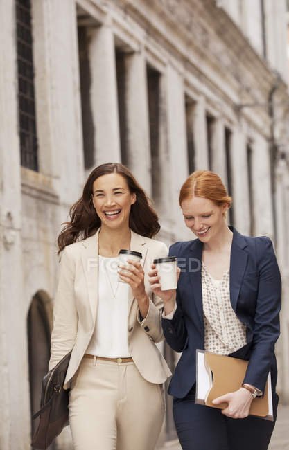 Mujeres sonrientes caminando con café - foto de stock