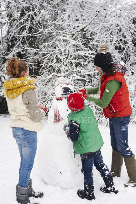 Mother and children making snowman outdoors — Stock Photo