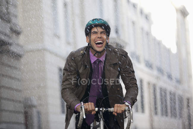Enthusiastic businessman riding bicycle in rain — Stock Photo