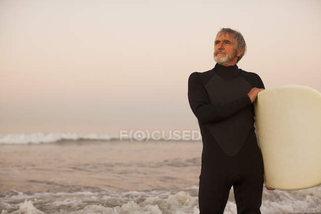 Older surfer carrying board on beach — Stock Photo