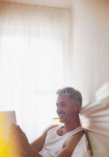 Homem sorridente usando tablet digital na cama — Fotografia de Stock