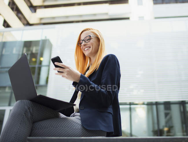Mujer de negocios sentada en el banco usando el teléfono celular - foto de stock