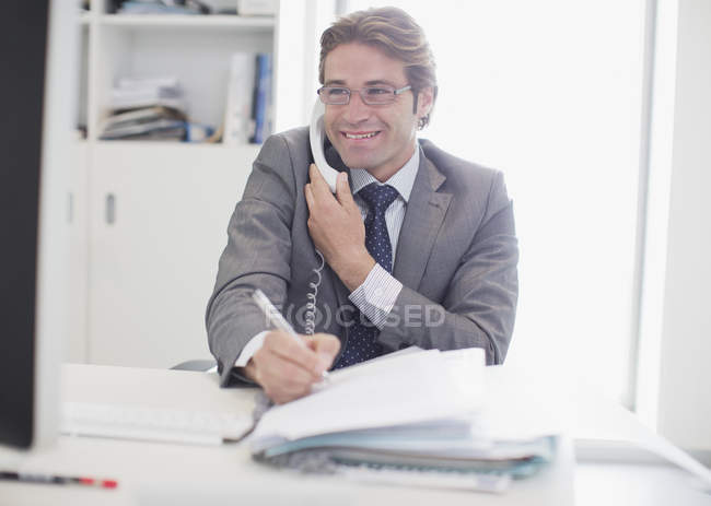 Empresário sorridente falando por telefone e escrevendo — Fotografia de Stock