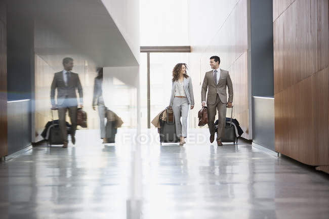 Бізнесмен і бізнес-леді тягнуть валізи через коридор — стокове фото