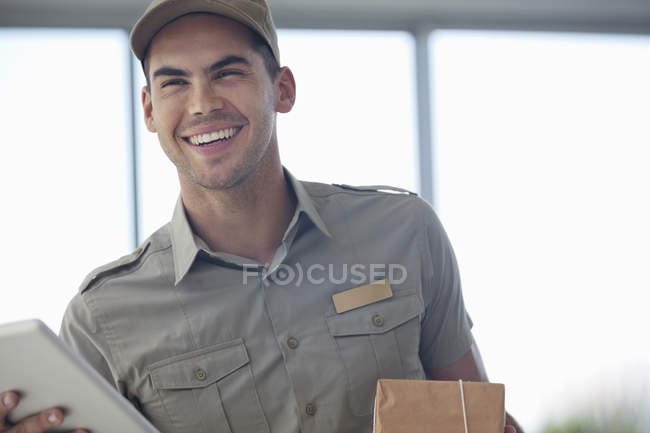 Zusteller lächelt mit Paket im modernen Büro — Stockfoto