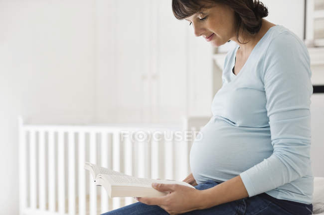 Pregnant woman reading in nursery — Stock Photo