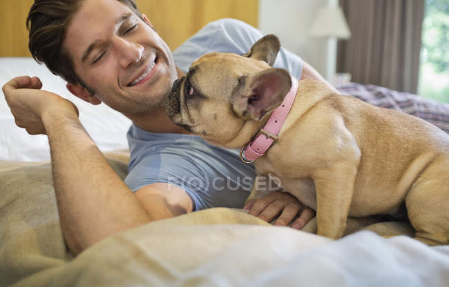 Cão lambendo mans rosto na cama em casa moderna — Fotografia de Stock