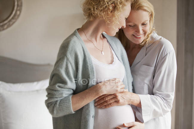 Mère tenant l'estomac de sa fille enceinte — Photo de stock