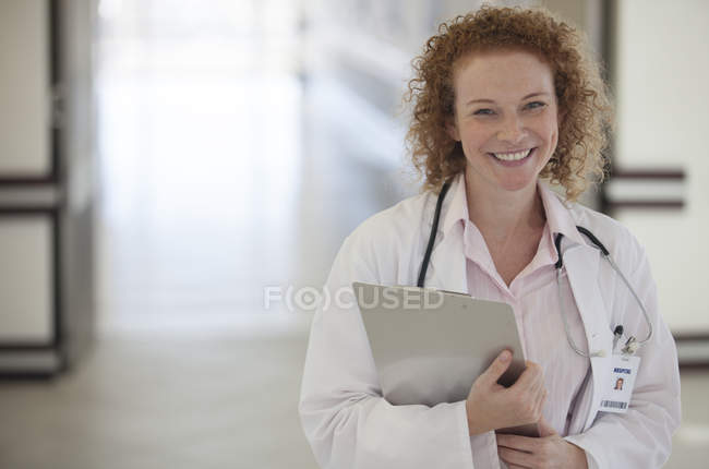 Doctor llevando portapapeles en el pasillo del hospital - foto de stock