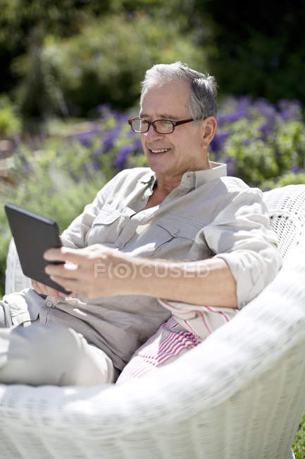 Homem sênior usando tablet digital em poltrona — Fotografia de Stock