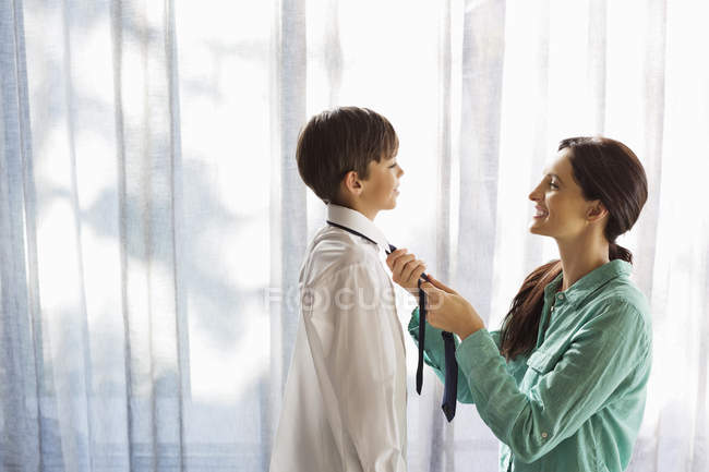 Mãe amarrando gravata do filho na janela — Fotografia de Stock