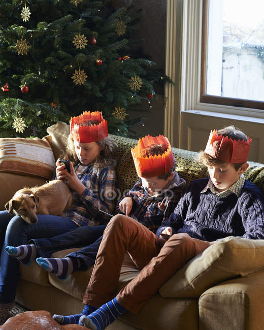 Niños en coronas de papel relajándose en el sofá - foto de stock