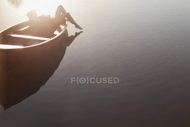 Mulher deitada em barco no lago ensolarado — Fotografia de Stock