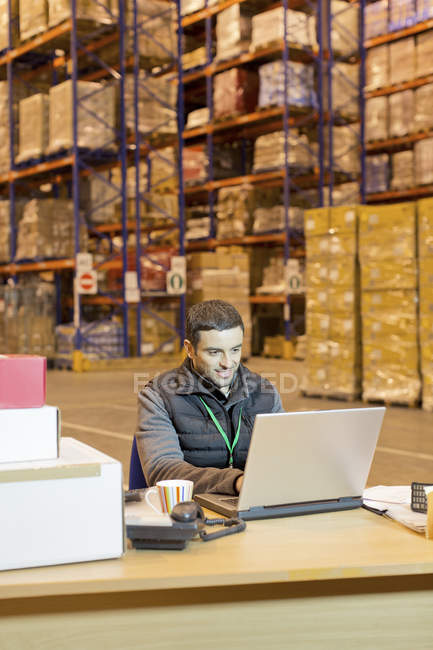Worker using laptop in warehouse — Stock Photo