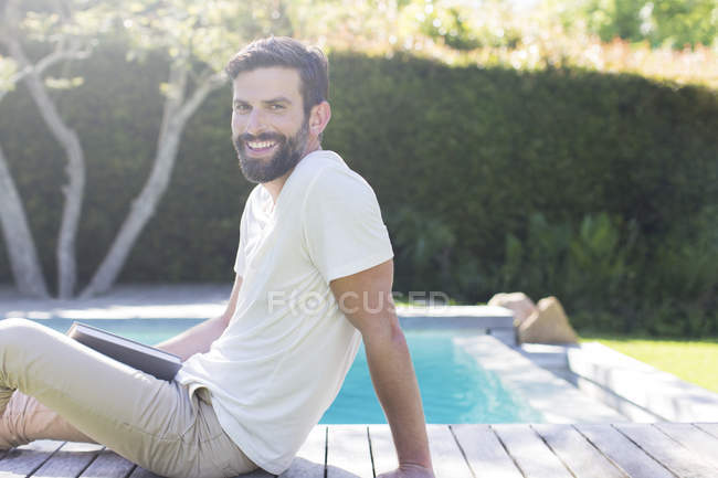 Hombre sonriente relajándose en la cubierta de madera junto a la piscina - foto de stock
