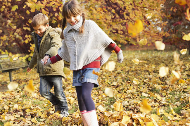Niños felices jugando en hojas de otoño - foto de stock