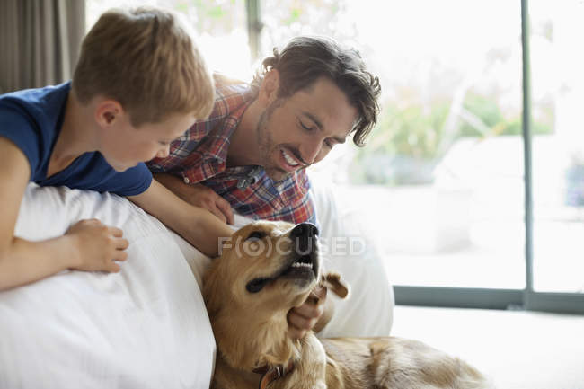 Padre e hijo acariciando perro en sofá - foto de stock