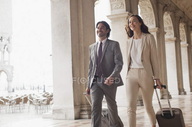 Homme d'affaires souriant et femme d'affaires tirant des valises le long du couloir — Photo de stock