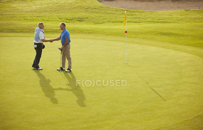 Старшие мужчины пожимают руки на поле для гольфа — стоковое фото