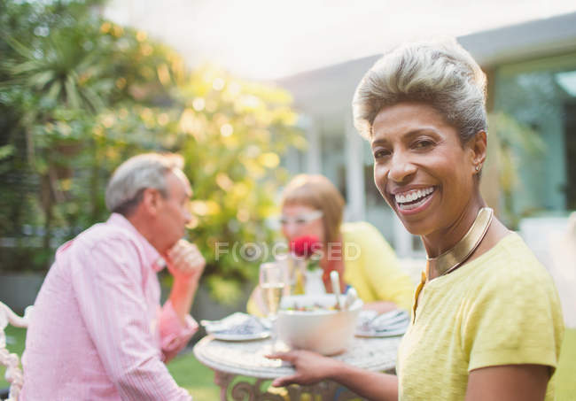 Retrato sonriente mujer madura disfrutando del almuerzo con amigos en el jardín - foto de stock