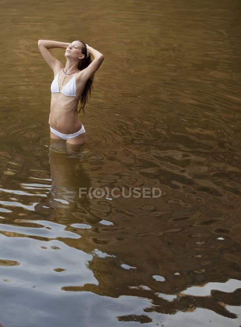 Женщина, стоящая с руками в волосах в реке — стоковое фото