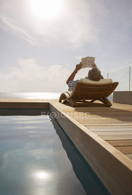 Homme lisant dans la pelouse chaise près de la piscine — Photo de stock