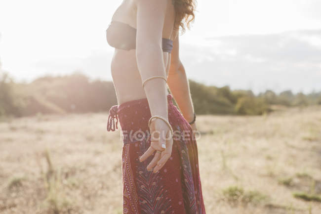 Boho woman in bikini top and skirt with arms outstretched in sunny rural field — Stock Photo
