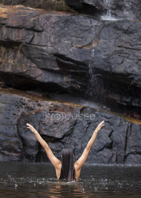 Woman standing in pool with arms outstretched — Stock Photo