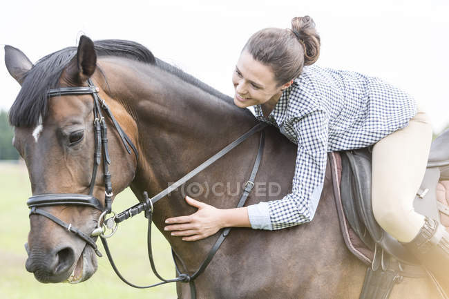 Smiling woman horseback riding leaning and petting horse — Stock Photo