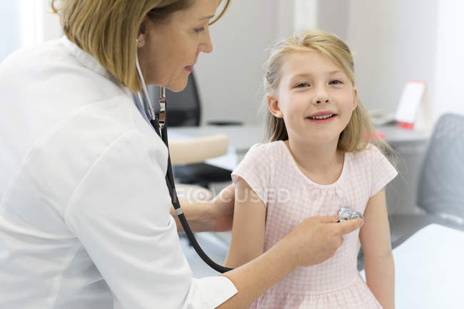Pediatra usando estetoscopio en paciente niña en sala de examen - foto de stock
