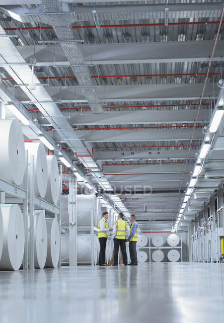Workers in reflective clothing talking near large paper spools in printing plant — Stock Photo