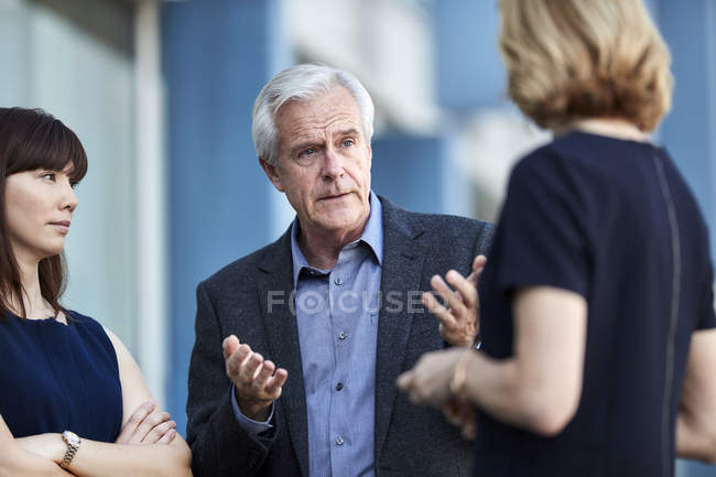 Empresario sénior gesticulando y hablando con colegas - foto de stock