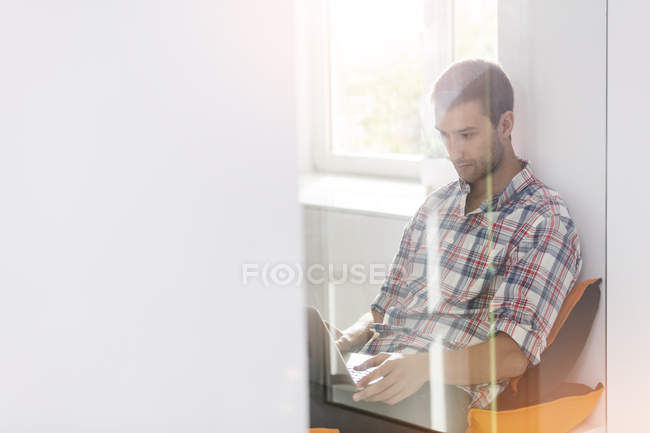 Homme d'affaires occasionnel utilisant un ordinateur portable dans la fenêtre du bureau — Photo de stock