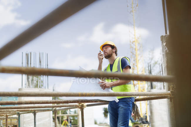 Engineer with blueprints using walkie-talkie at construction site — Stock Photo