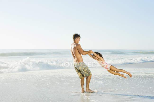 Father swinging daughter in surf at beach — Stock Photo