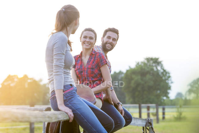 Smiling friends sitting on rural fence — Stock Photo