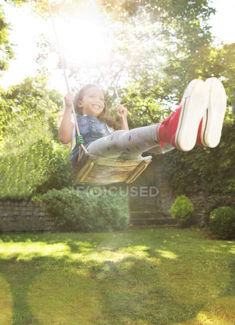 Fille enthousiaste balançant dans la cour ensoleillée — Photo de stock